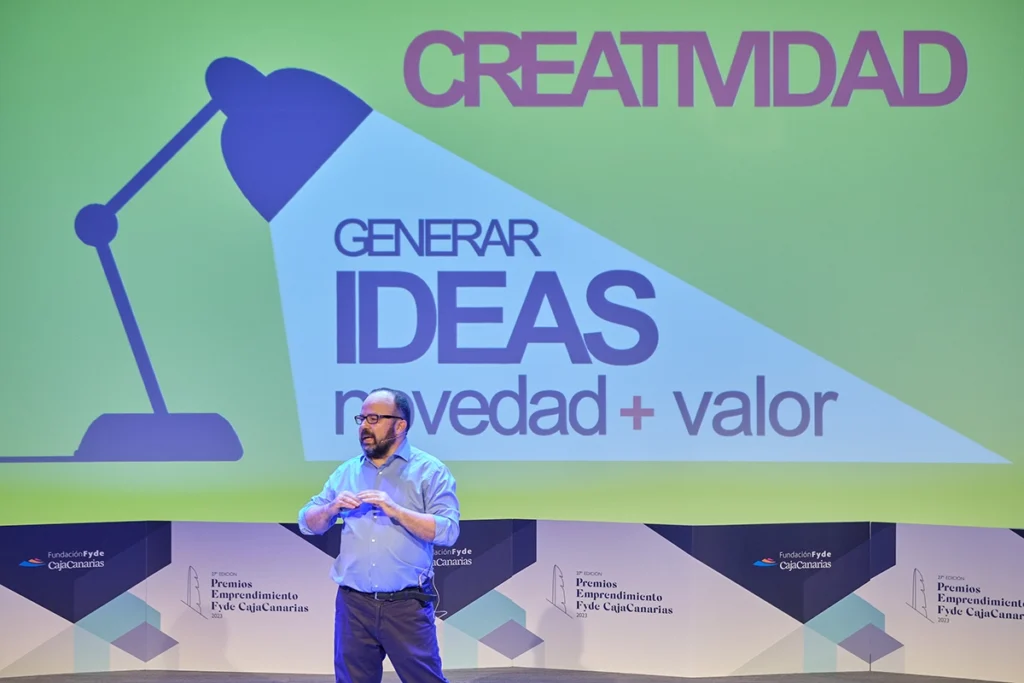 Juan Pastor Bustamante en un escenario durante una conferencia de creatividad en Canarias, con una diapositiva de “Generar ideas” al fondo.