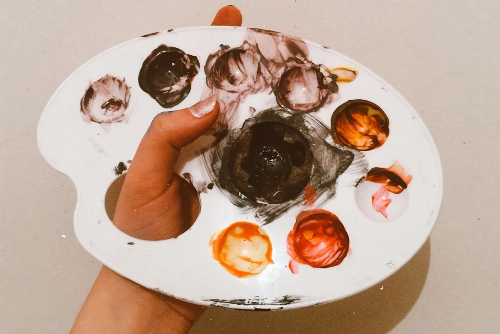 Mano sosteniendo una paleta de pintura con manchas de color, asociada a artistas y diseñadores.