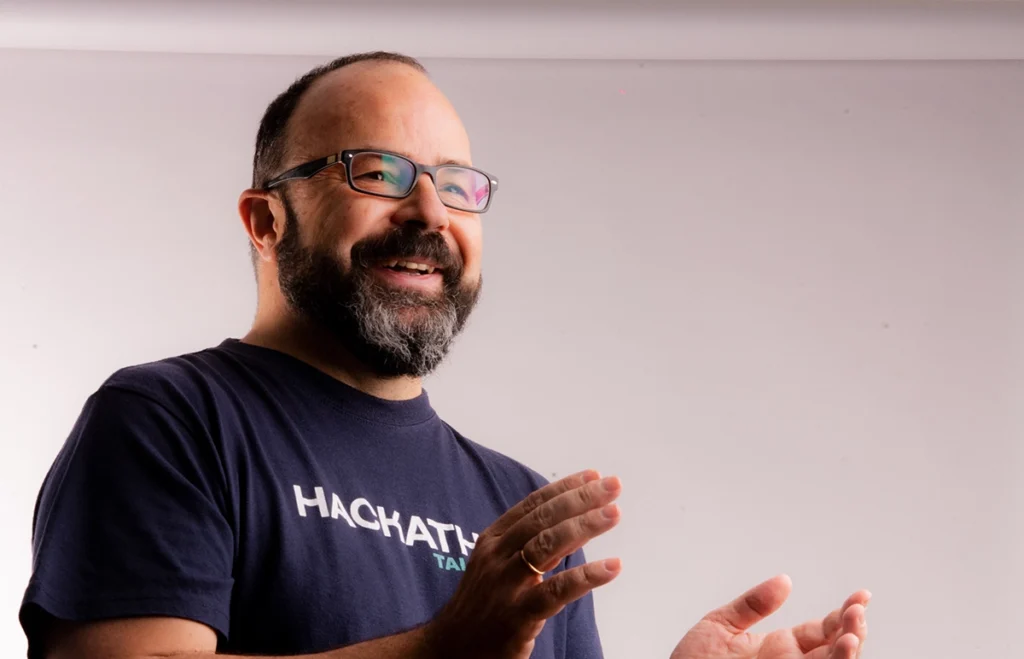 Juan Pastor Bustamante sonriendo mientras habla y gesticula, consultor de creatividad e innovación con camiseta oscura sobre fondo claro.