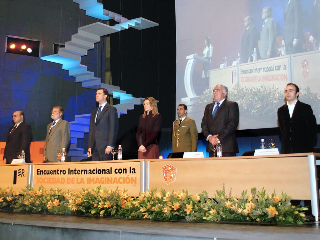 Escenario de un congreso con un panel de personas de pie tras una mesa y una pantalla de proyección al fondo.