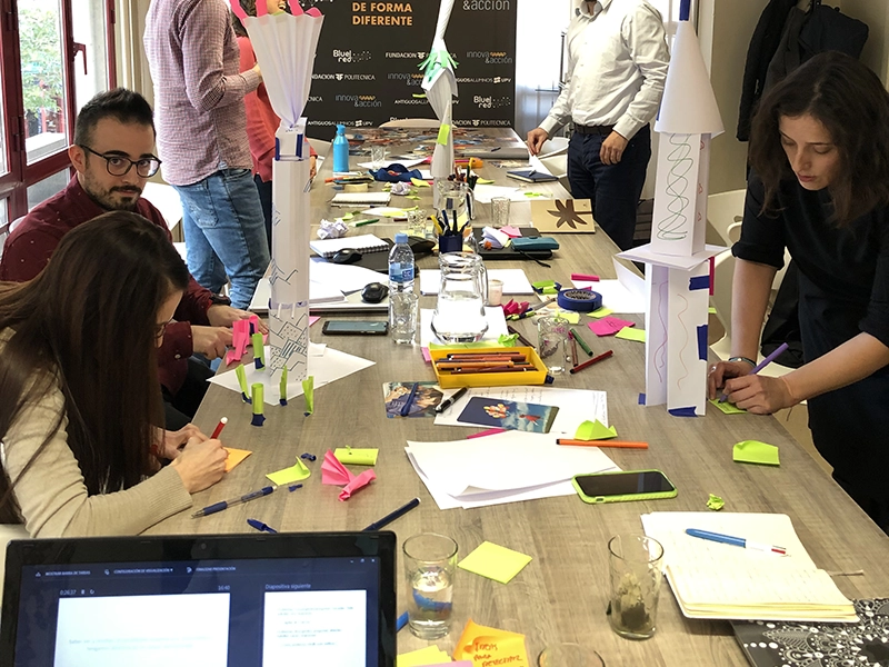 Taller de creatividad e innovación con equipo trabajando con post-its y prototipos en una mesa.
