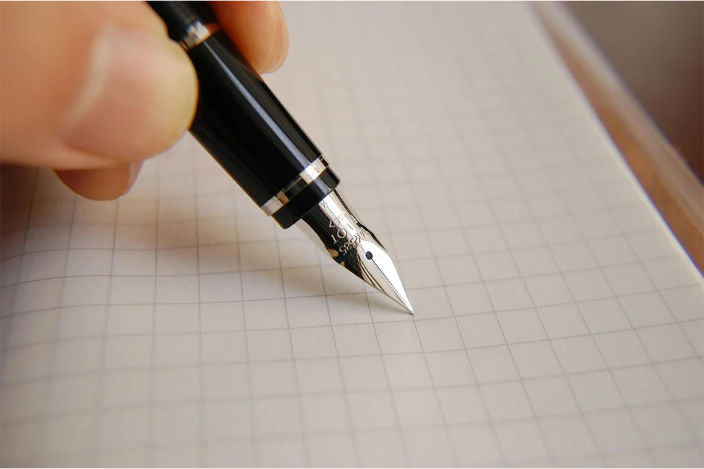 Pluma estilográfica sobre papel cuadriculado para anotar un diseño de programas.