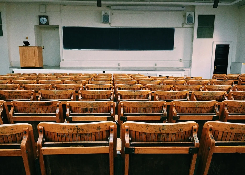 Aula universitaria vacía con filas de asientos de madera, pizarra grande y atril, asociada a innovación educativa.