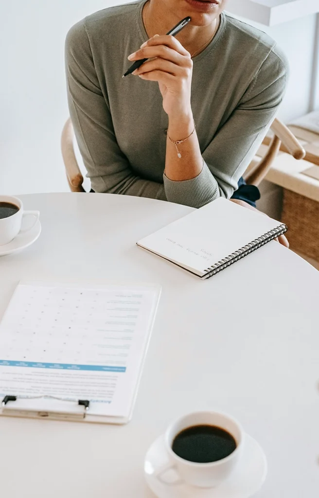 Persona con bolígrafo y cuaderno en una mesa con café, en una orientación práctica y realista.