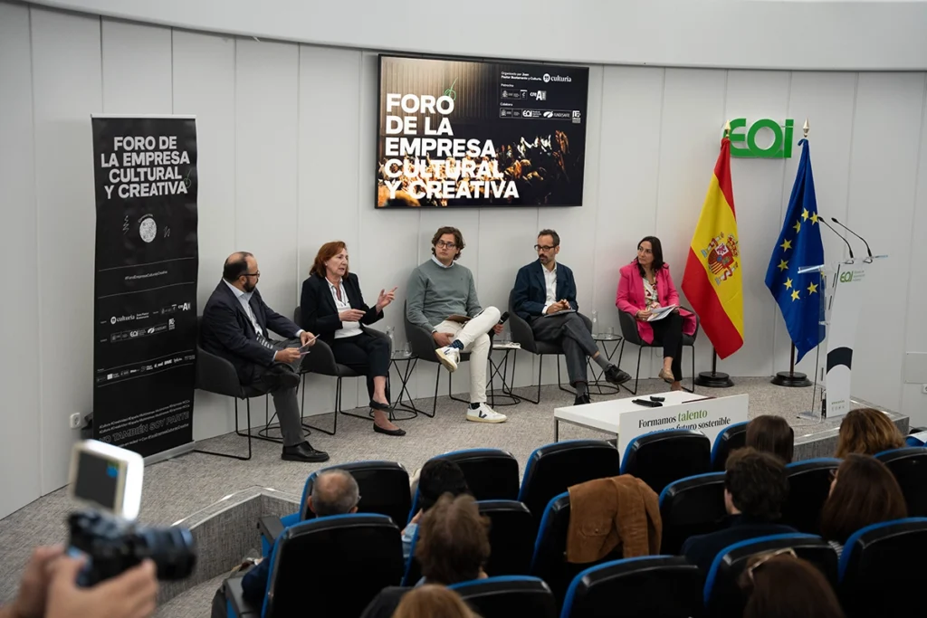 Mesa redonda en un auditorio sobre economía creativa e innovación, con ponentes sentados, entre ellos Juan Pastor Bustamante, y público asistiendo.