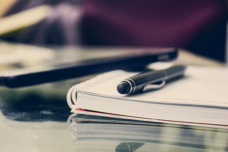 Bolígrafo sobre cuaderno con portátil desenfocado, preparando programas internos de innovación en empresas.