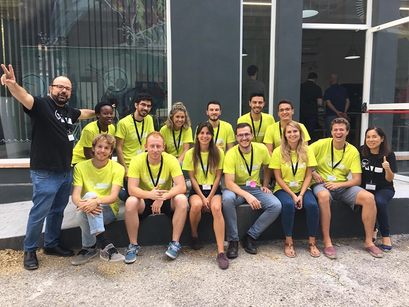 Foto de grupo de participantes con camisetas amarillas posando junto a Juan Pastor Bustamante en exterior durante un evento de innovación.